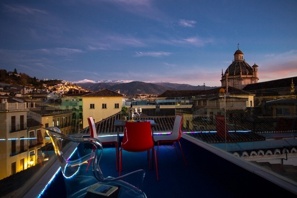 uma mesa e cadeiras em uma varanda com vista para uma cidade ao pôr do sol