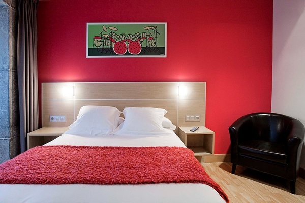 a bedroom with a red wall and a picture on the wall above the bed