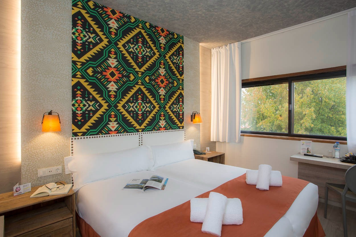 Gemütliches Zimmer im Casual Inca Porto: Doppelbett, bunte Wanddekoration und Fenster mit Blick ins Grüne.