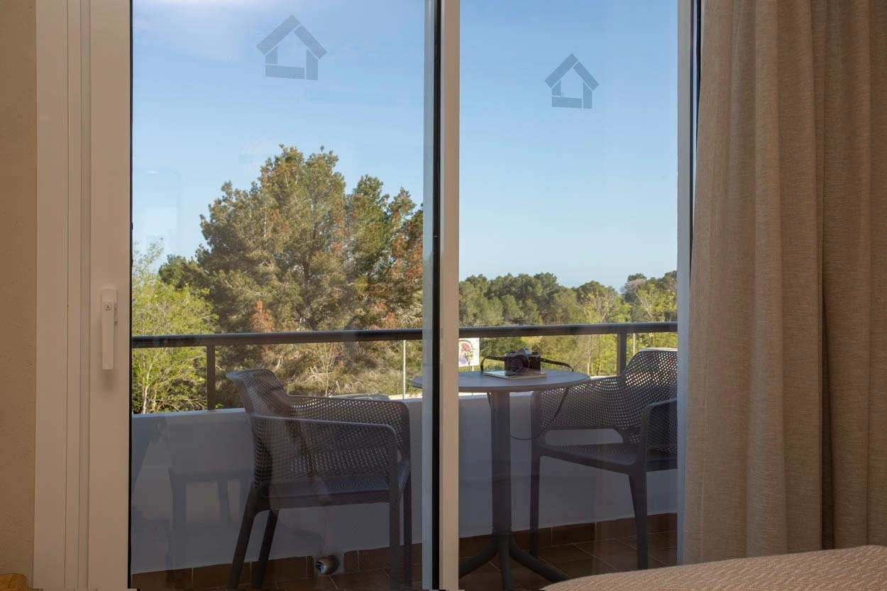 Balcon de chambre Casual Bahía Ibiza avec chaises et table, vue sur la verdure.