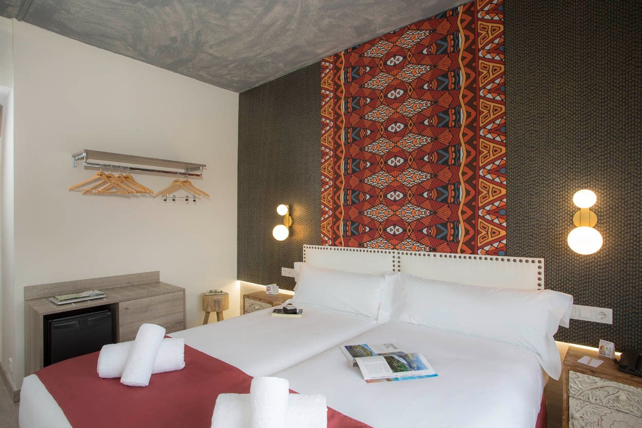 Zwei weiße Betten, bereit für Gäste im Casual Inca Porto, mit buntem Akzentwanddesign und modernen Lampen.