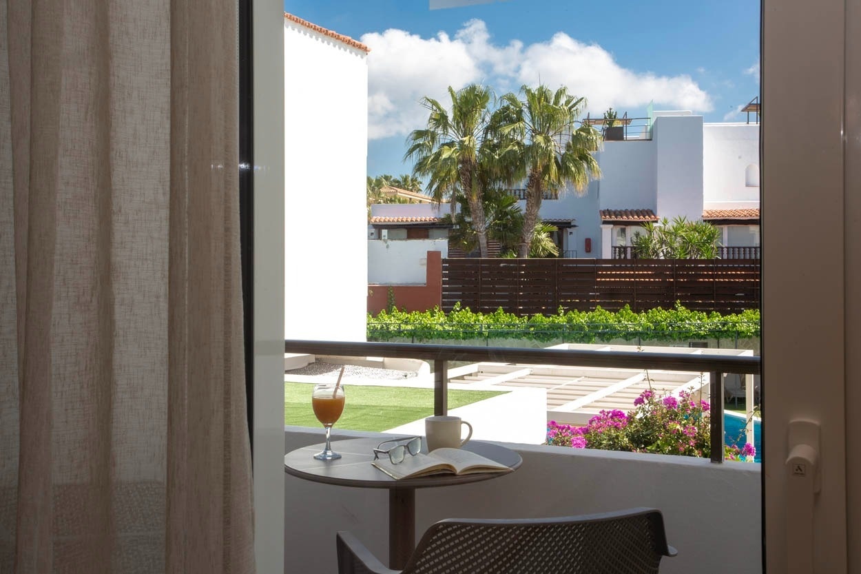 Vue depuis une chambre avec balcon de Casual Bahía Ibiza : jus, livre, tasse et vue sur le jardin et la piscine.