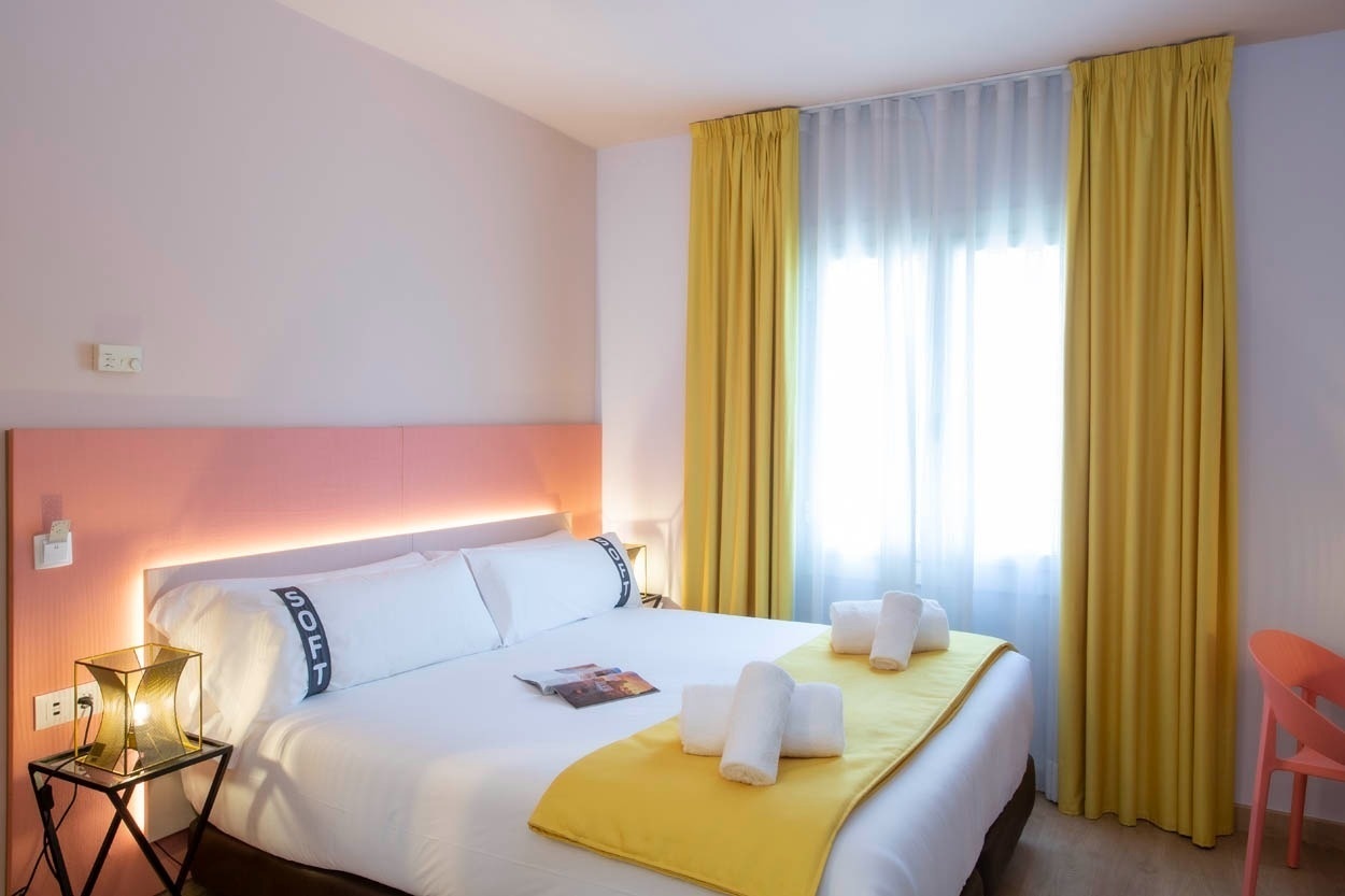 Een slaapkamer in Casual Colours Barcelona met een comfortabel bed, gele gordijnen en een roze hoofdbord, gelegen in de buurt van Sants.