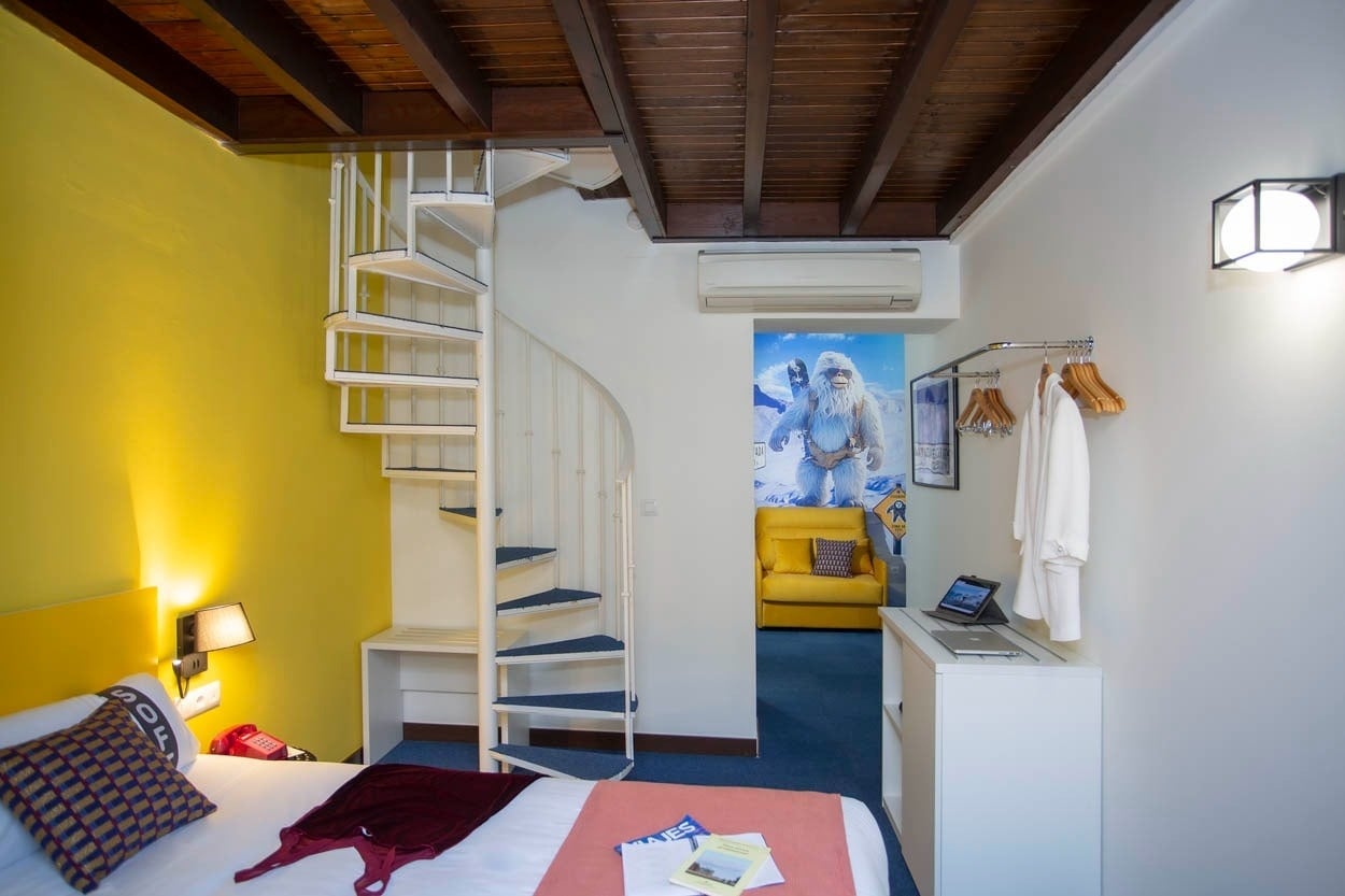 Habitación temática con escaleras de caracol, arte mural de Yeti y sofá amarillo en Casual Ilbira Granada.