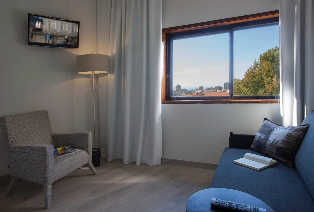 Modernes Hotelzimmer mit Sofa, Sessel und Fensterblick im Casual Inca Porto