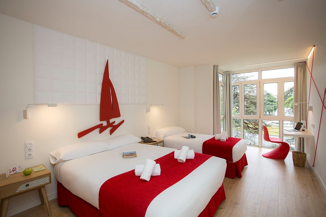 Doppelzimmer im Casual de las Olas San Sebastián mit zwei Betten, roten Akzenten und Meerblick.