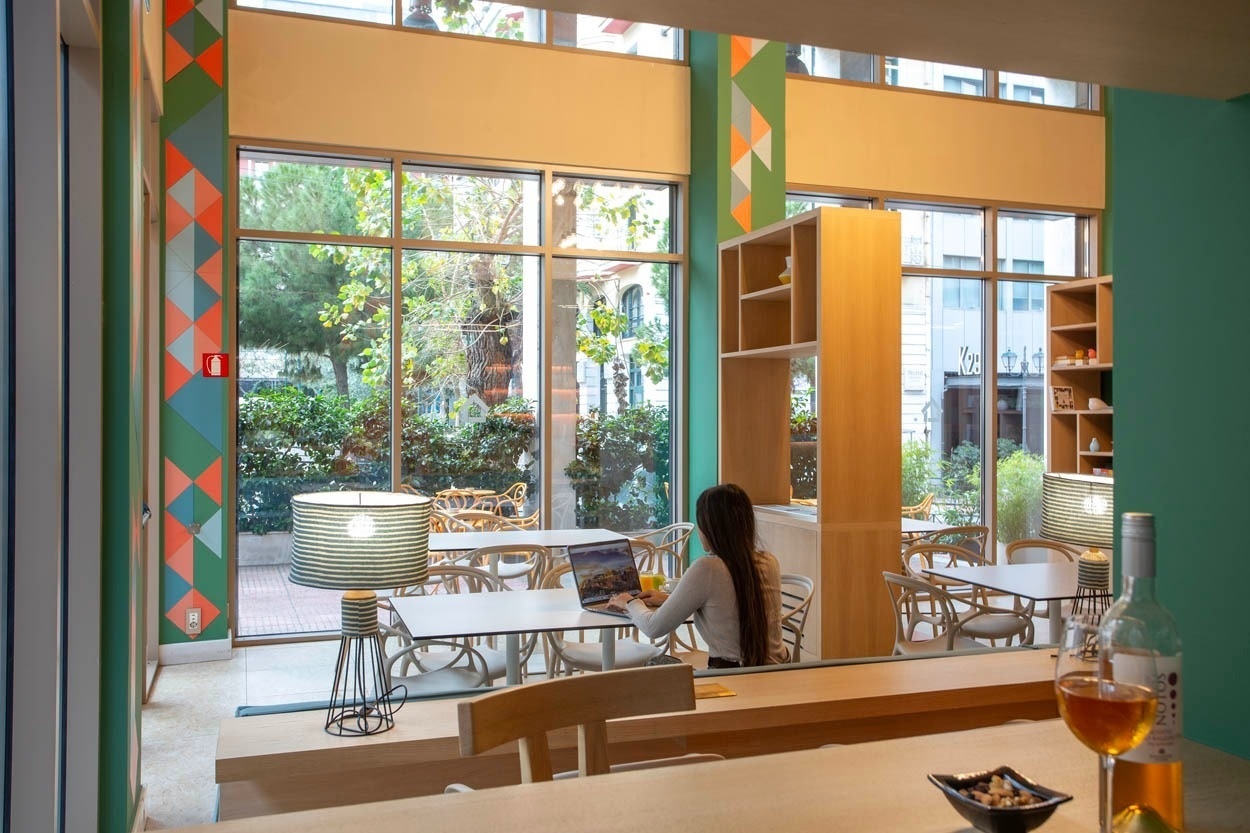 Frau arbeitet am Laptop im Casual Kubic Athens, einem modernen Hotel im Zentrum von Athen mit hellem Innenraum und Gartenblick.