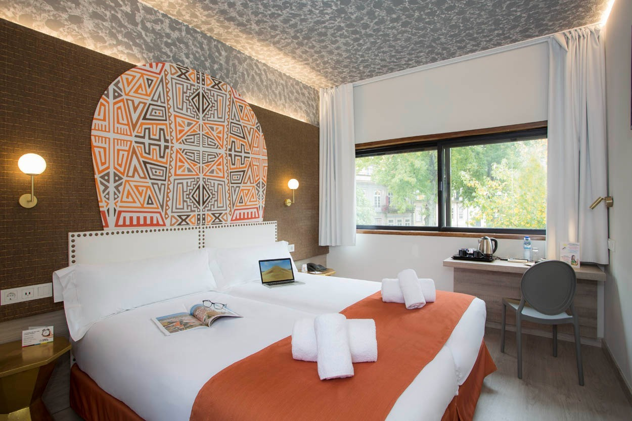 Modernes Hotelzimmer im Casual Inca Porto, mit Doppelbett, Blick ins Grüne und stylischem Kopfende.