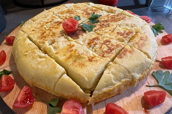 uma tortilha é cortada em pedaços e está sobre uma tábua de madeira com tomates e ervas