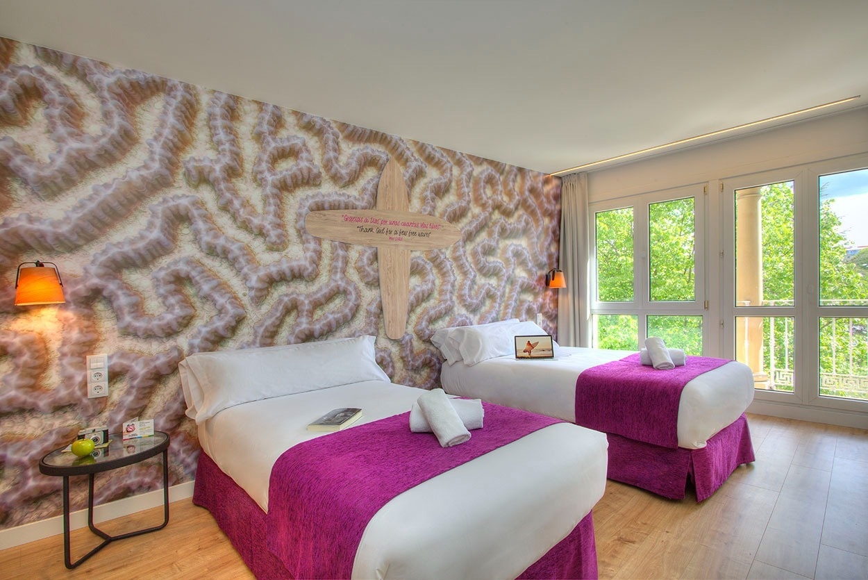 Gemütliches Schlafzimmer im Casual de las Olas San Sebastián, Themenhotel mit Korallenwand und lila Akzenten.