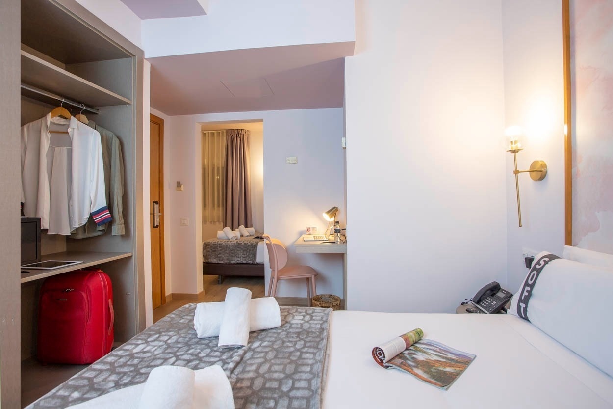 Stijlvolle hotelkamer met garderobekast, kleding en rode koffer. Casual Colours Barcelona - Hotel nabij Sants.