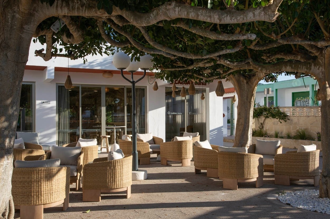 Terrasse ombragée avec fauteuils en osier et vue sur la façade du Casual Bahía Ibiza, hôtel près de la plage.