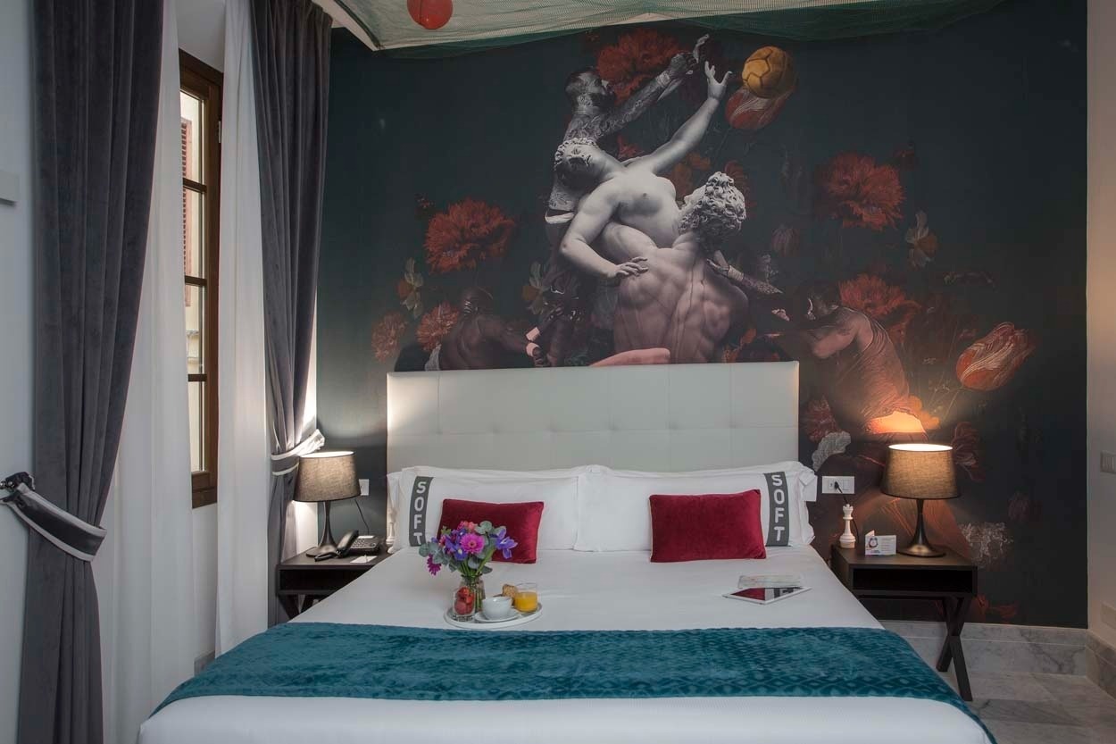 Luxuriöses Zimmer im Casual Rinascimento Firenze: Bett mit Kunst-Wandgemälde, Sitzgelegenheit und Nachtisch.