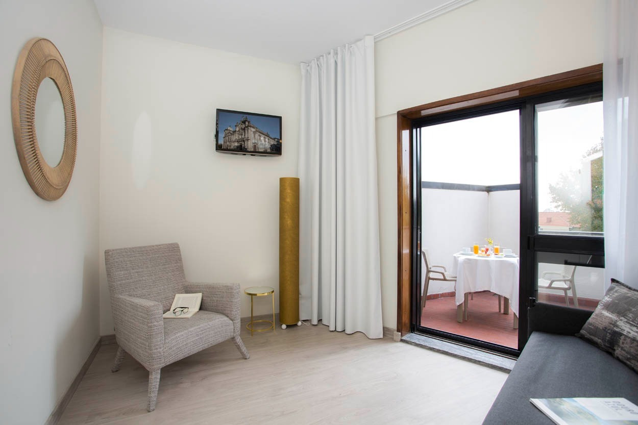 Gemütliches Zimmer im Casual Inca Porto: Sessel, Spiegel, Balkon & Frühstückstisch.