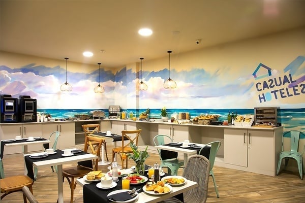una habitación llena de mesas y sillas con un mural en la pared que dice casual hotel