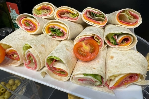 un plato blanco lleno de wraps y un tomate junto a una botella de aceite de oliva