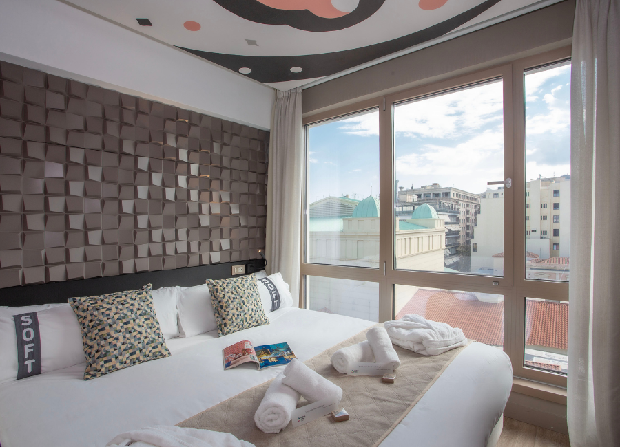 Modern hotel room with stylish textured headboard and large window offering city views.