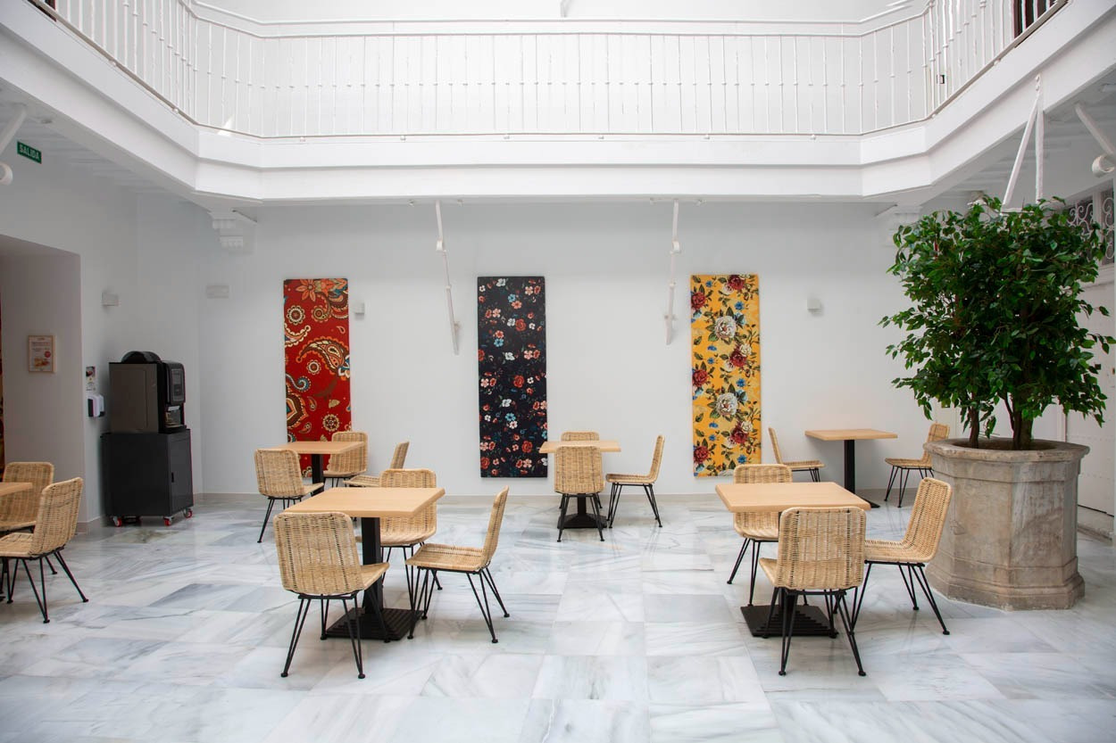 Gemütlicher Innenhof des Casual con Duende Cádiz – Hotel im Zentrum. Elegante Tische und Stühle mit Kunst.