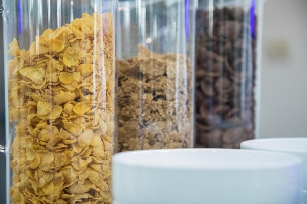 a glass jar filled with corn flakes next to a bowl of cereal