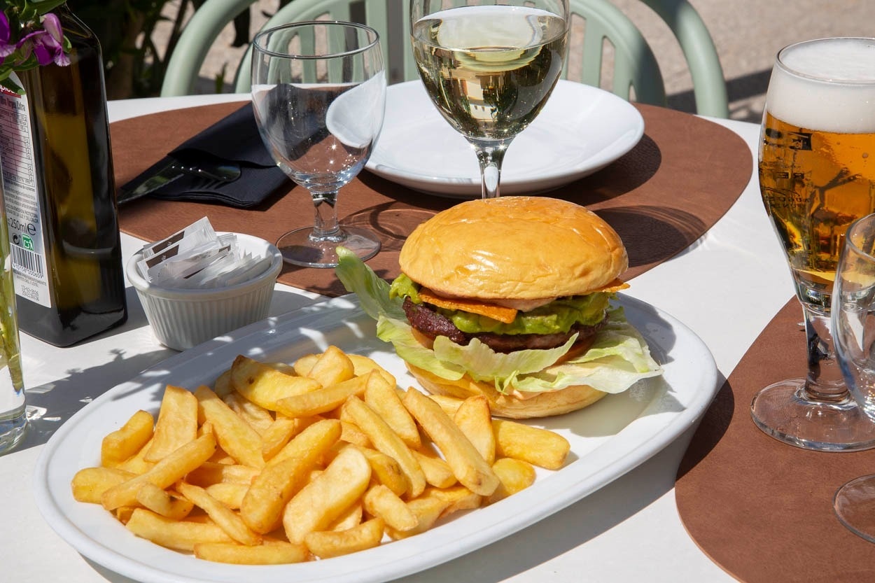 Un hamburger avec des frites est servi sur une table d'extérieur, accompagné de diverses boissons.
