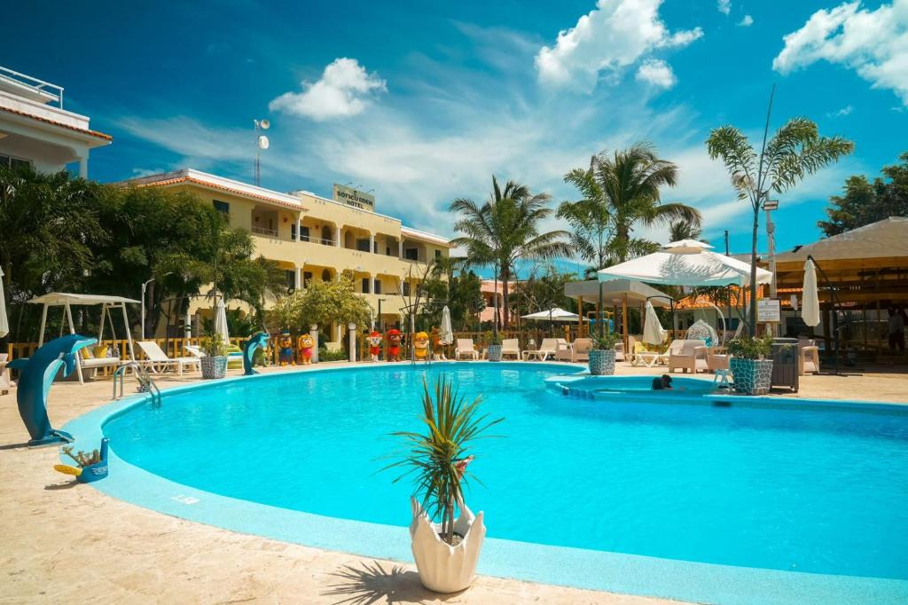 Piscina luminosa e soleggiata presso Casual: Corporativa con lettini, palme e hotel sullo sfondo