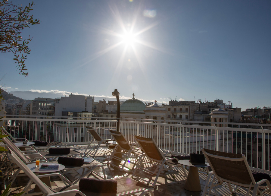 Sunny hotel rooftop terrace with sun loungers, city views, and bright sky, ideal for relaxation.