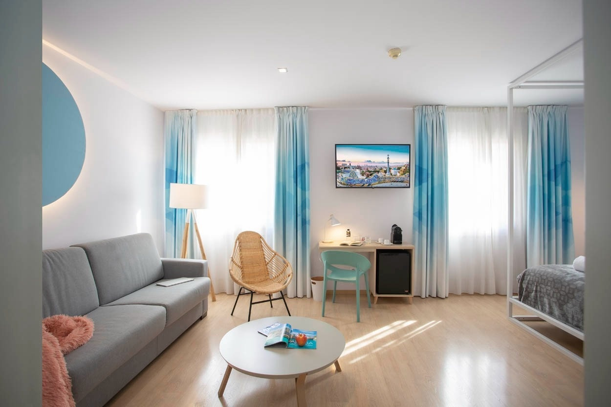 Lichte hotelkamer met bank, rieten stoel en blauwe gordijnen bij Casual Colours Barcelona - Hotel in de buurt van Sants in Barcelona | Casual Hoteles.