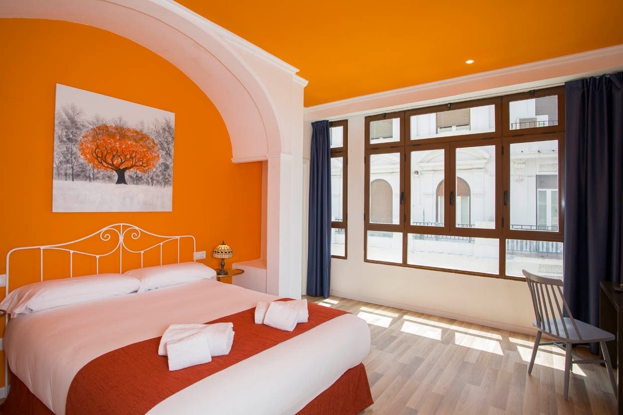Cama matrimonial con cabecero blanco y cuadros de árbol en hotel Casual Valencia, cerca del Ayuntamiento.