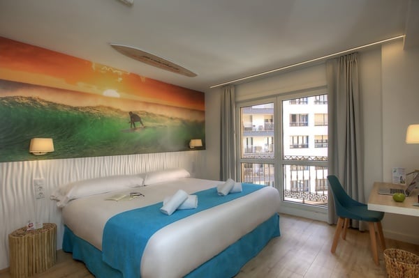 um quarto de hotel com uma cama king size e uma prancha de surf na parede