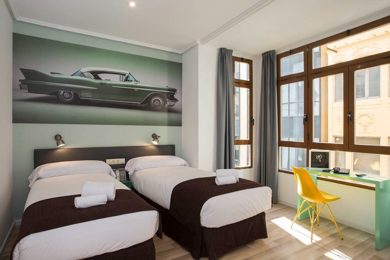 Habitación doble Casual Vintage Valencia con mural de coche clásico, mesas de noche, escritorio y silla amarilla. Ideal Hotel céntrico junto al Ayuntamiento | Casual Hoteles