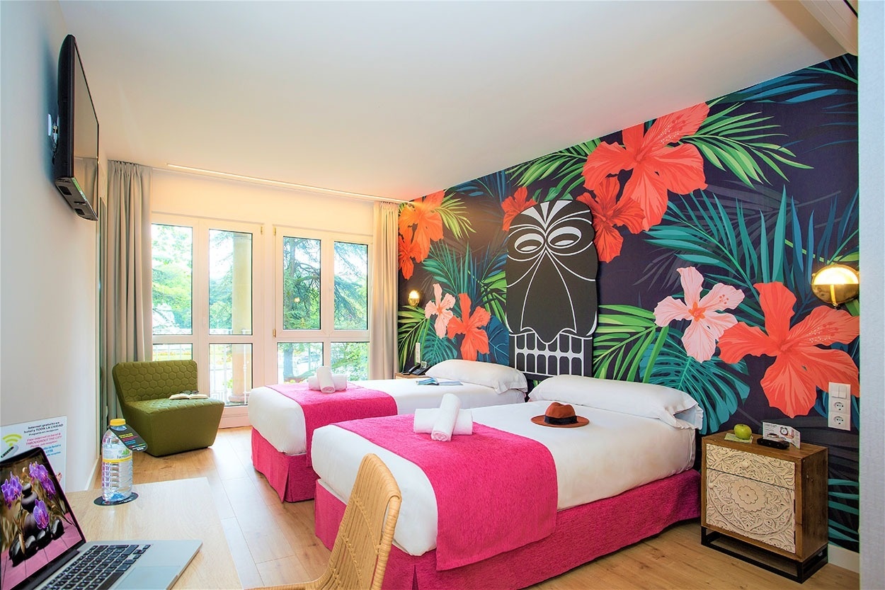 Gemütliches Doppelzimmer mit tropischem Wandbild im Casual de las Olas San Sebastián – Themenhotel. Ideal für einen entspannten Aufenthalt in San Sebastián.