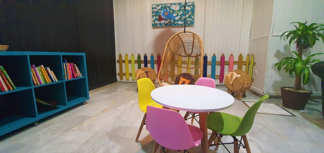 Kinderbereich im Casual de las Letras Sevilla: Bunte Stühle, Tisch und Hängesessel für Spaß.