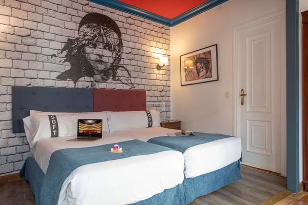 een hotelkamer met twee aparte bedden en een muurschildering van een gezicht en de woorden scott op de kussens