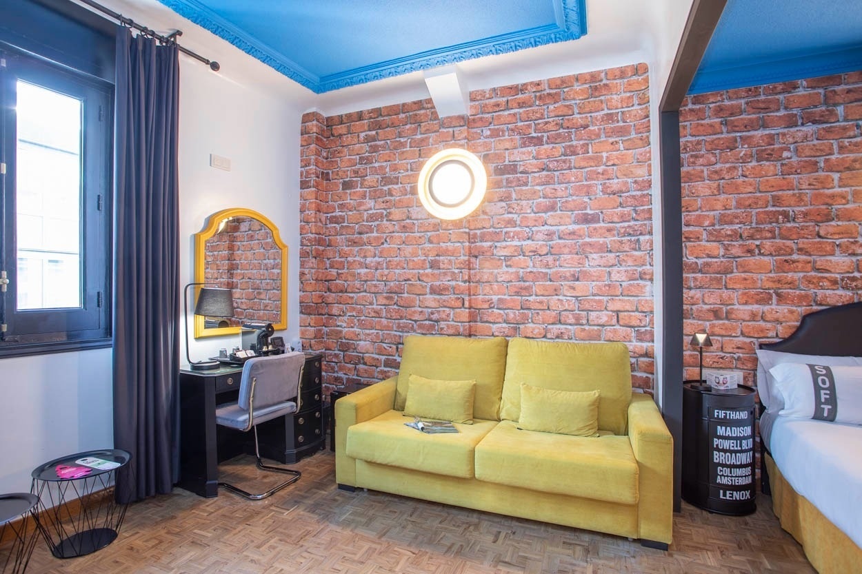 Gemütliches Zimmer mit gelber Couch und Backsteinwand im Casual del Teatro Madrid - Boutique-Hotel nahe der Gran Vía.