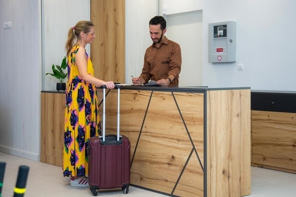 a woman with a suitcase is standing at a counter with a man in a brown shirt that says osiris