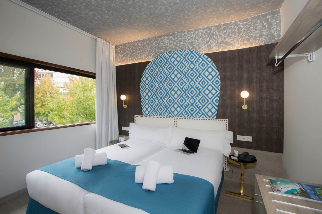 Modernes Doppelzimmer im Casual Inca Porto mit blauer Tagesdecke und Laptop.
