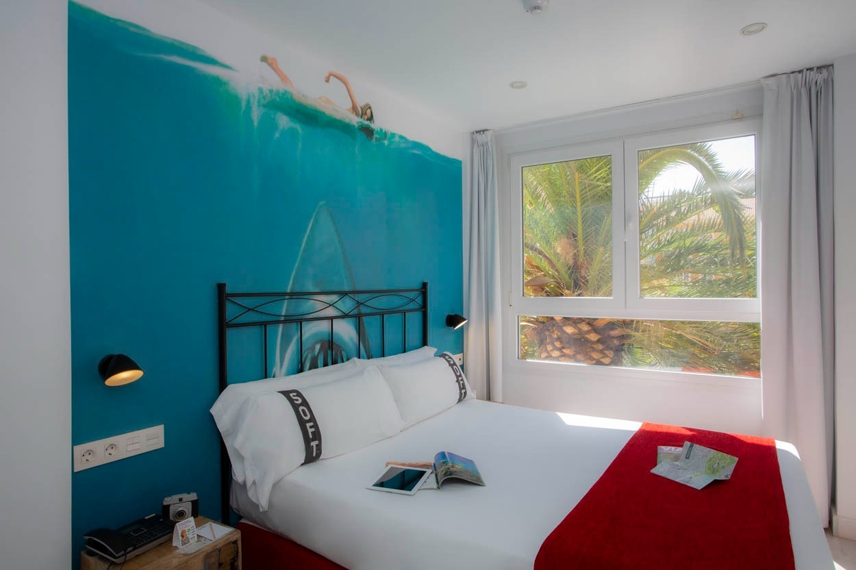 Modernes Doppelzimmer im Casual del Mar Málaga mit Surf-Wandgemälde und Meerblick vom Fenster.
