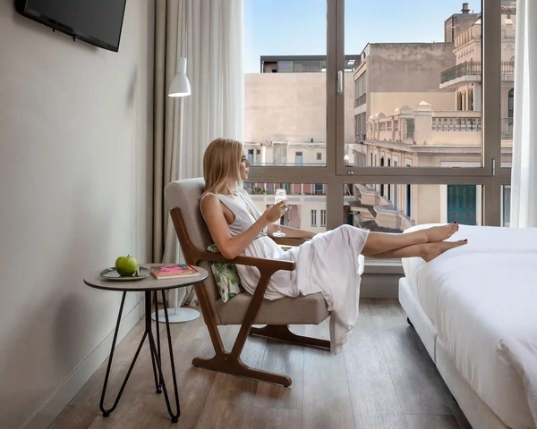 een vrouw zit in een stoel in een hotelkamer met een glas wijn