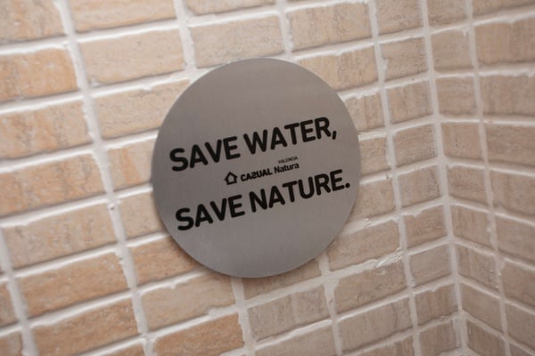una señal de acero inoxidable en una pared de ladrillo que dice guardar agua y salvar la naturaleza