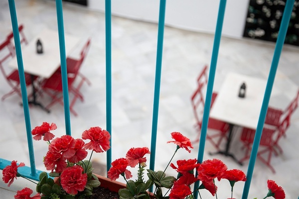un balcón con mesas y sillas rojas y flores rojas