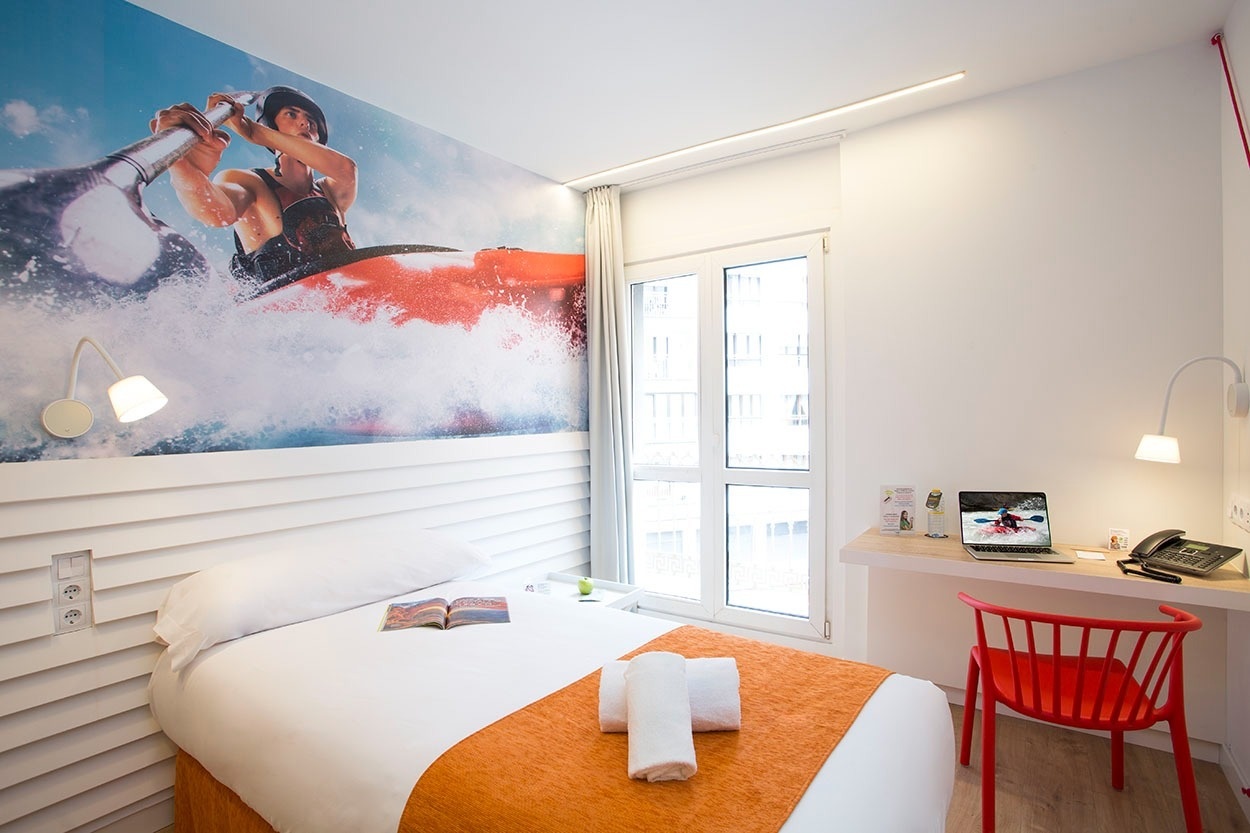 Modernes Hotelzimmer im Casual de las Olas San Sebastián mit Kayak-Motiv und orangefarbenen Akzenten.