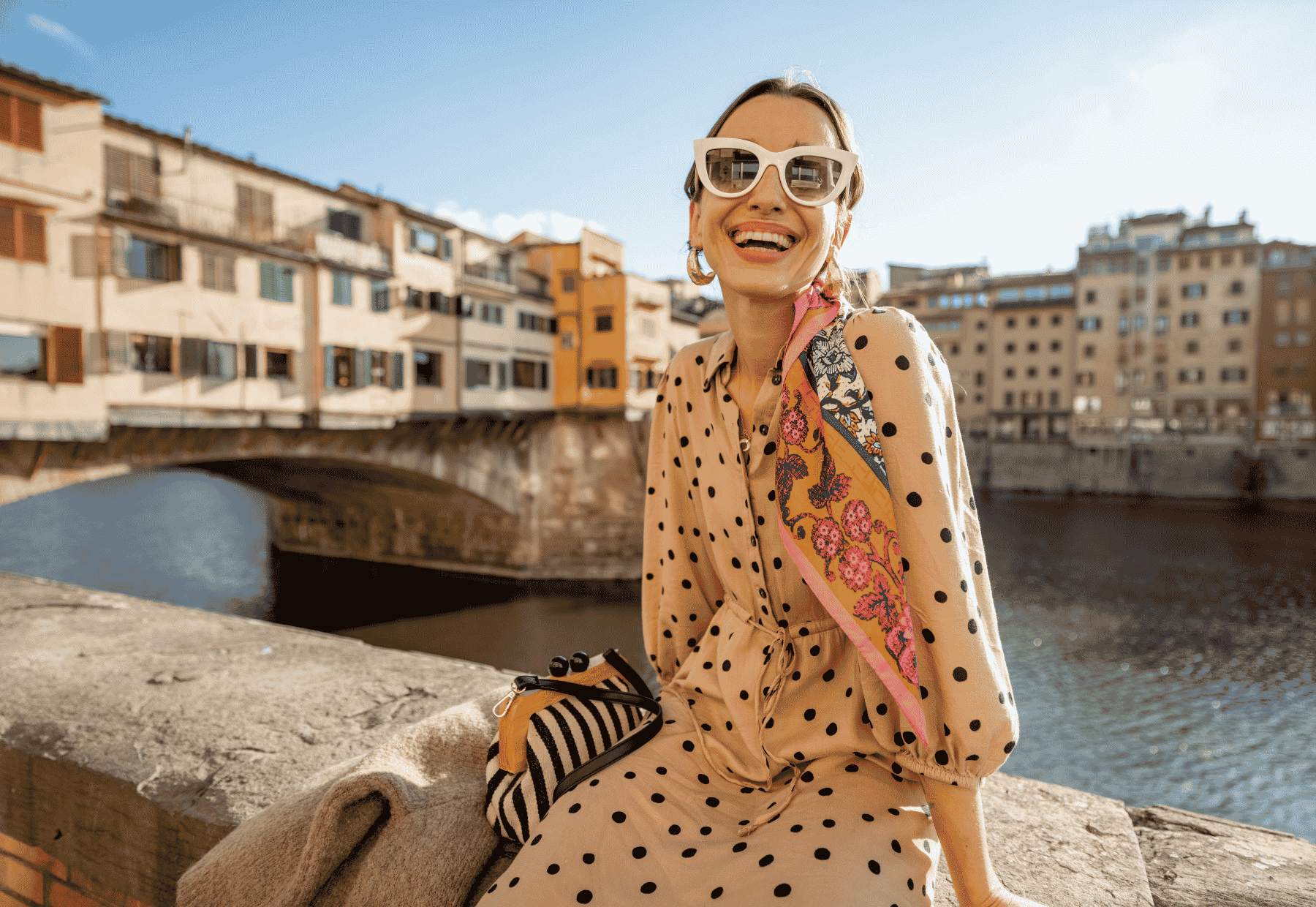 Donna sorridente con occhiali da sole bianchi e abito a pois su un ponte Settimana della Moda di Milano 2026: date e percorso della moda a Milano a Firenze