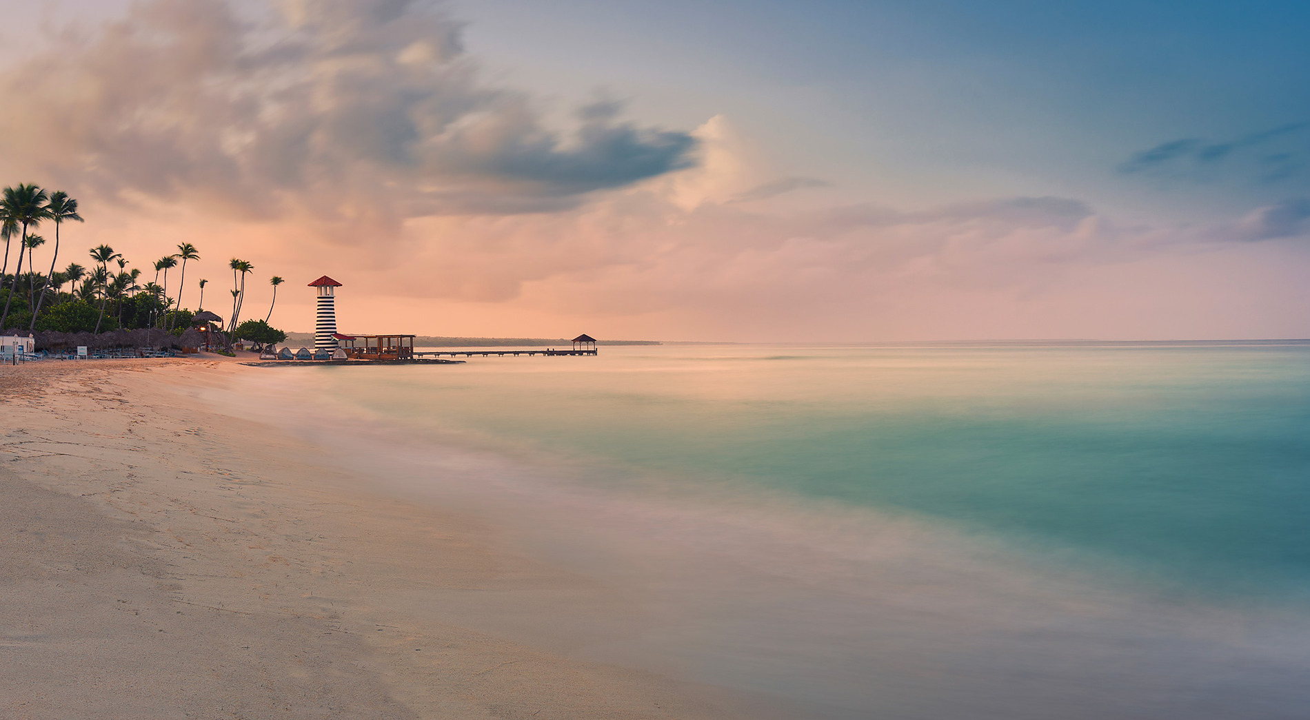 Atardecer en la playa de Bayahíbe con el faro a rayas y el embarcadero sobre aguas turquesas. Hoteles en Bayahíbe · Casual Hoteles · Web Oficial.