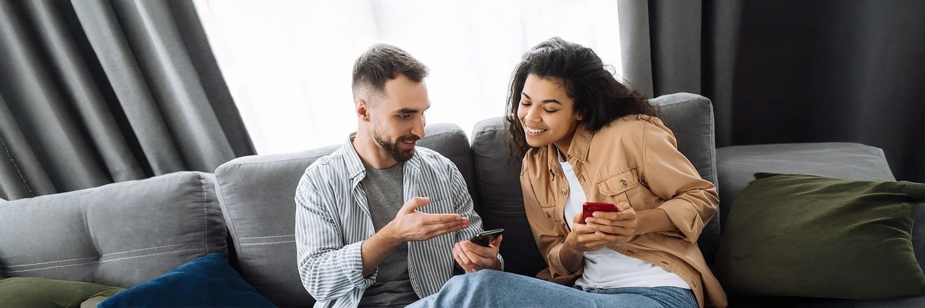 um homem e uma mulher estão sentados em um sofá olhando para seus telefones celulares