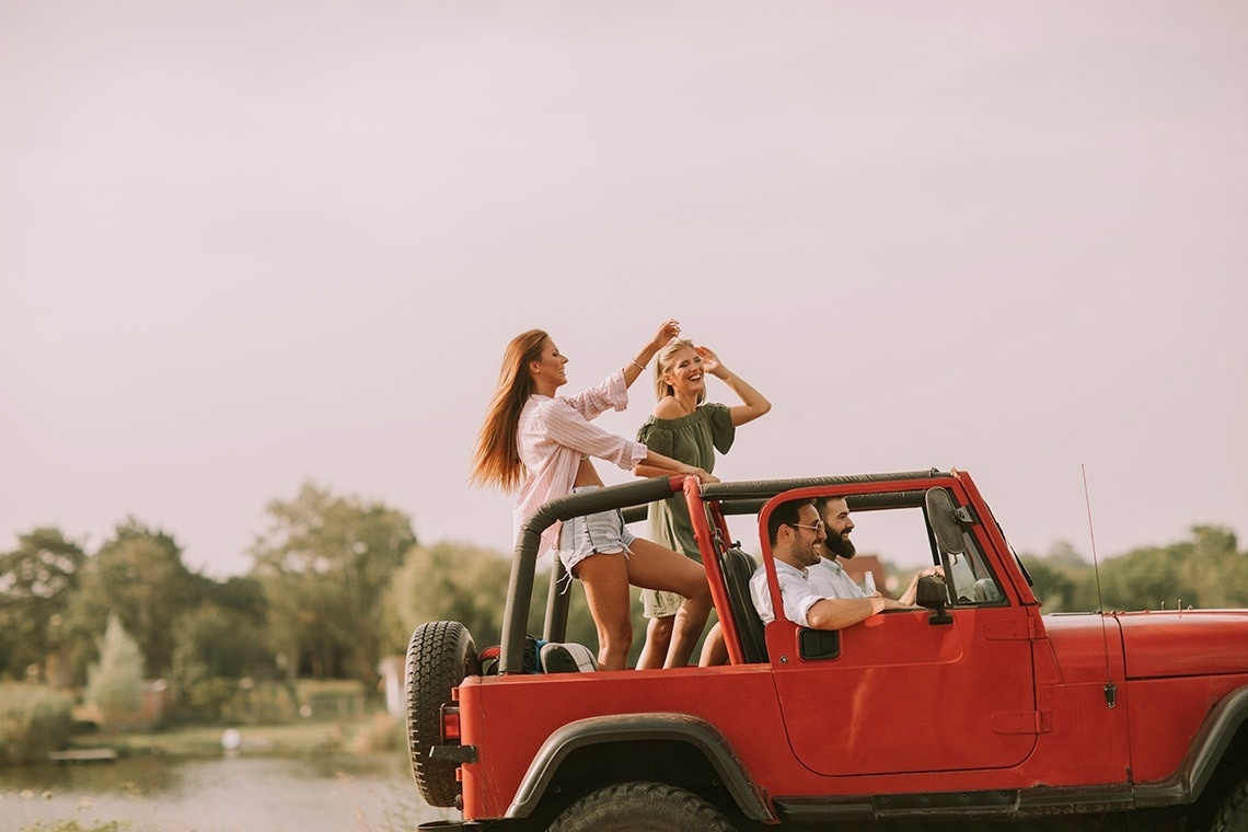 een man en twee vrouwen dansen in een rode jeep