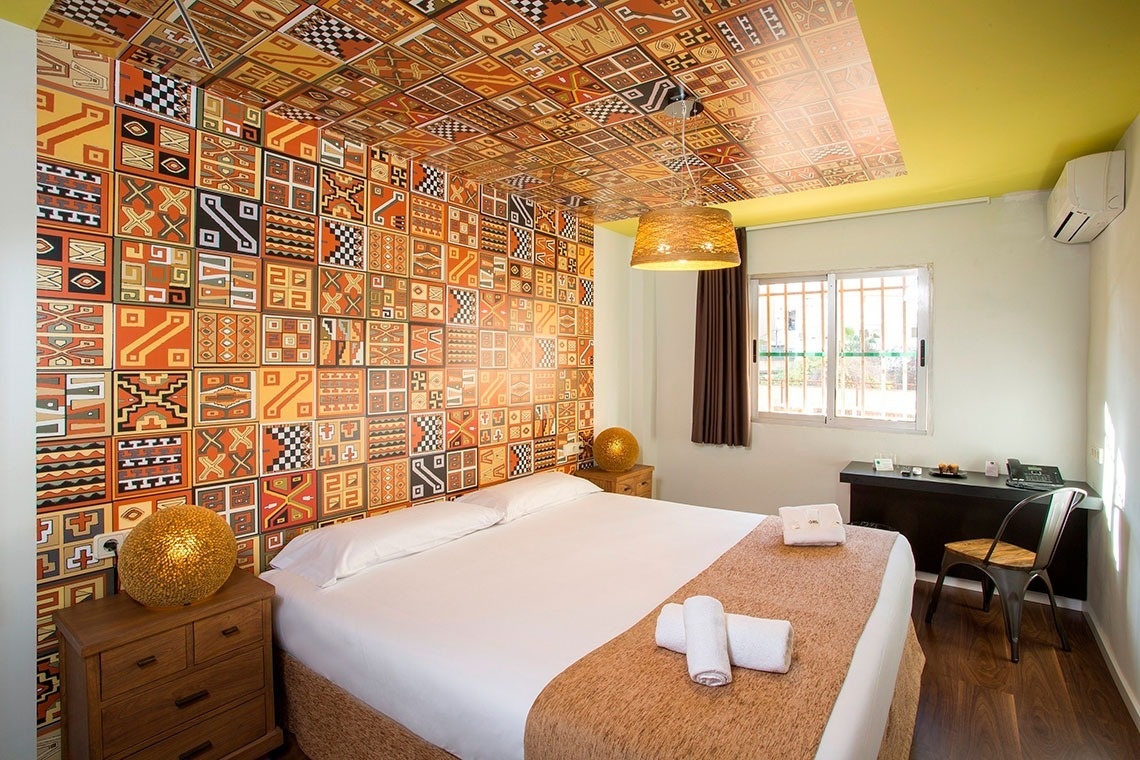 Bequemes Bett im Casual de las Civilizaciones Hotel in Valencia mit farbenfroher Wand- und Deckenverkleidung.