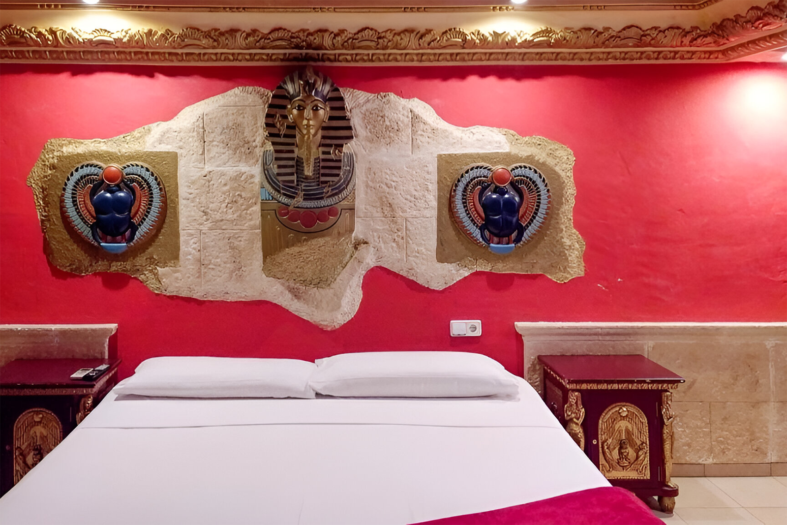 Ägyptisches Thema im Casual de las Civilizaciones - Günstiges Hotel Valencia. Dekorative Pharaonenmasken und Skarabäen über einem Bett.