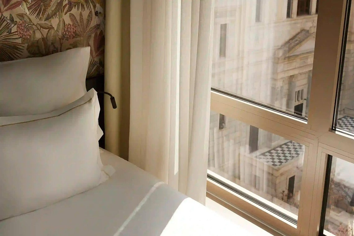 una cama junto a una ventana con una vista de un edificio