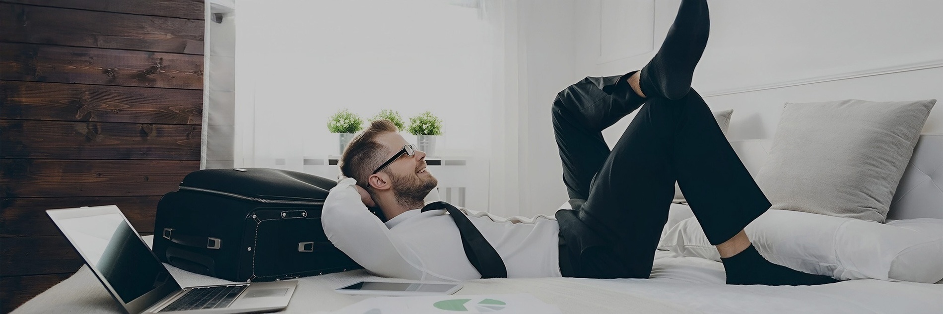 a man laying on a bed with a suitcase and a laptop