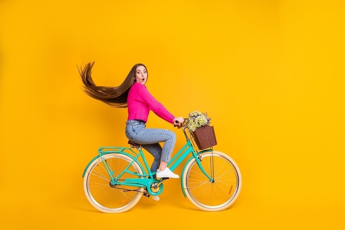 una mujer con cabello largo monta una bicicleta azul con una canasta de flores .